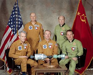 the five crew members of ASTP sitting around a miniature model of their spacecrafts