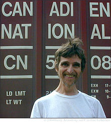 A man wearing a white t-shirt stands with the words "Canadien National" visible behind him.