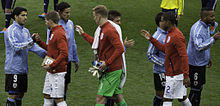 Gerrard, in a red jersey and white shorts, shaking hands with Uruguayan players in 2014