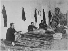 Black and white photo of three men weaving wicker baskets