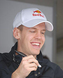 Sebastian Vettel signs an autograph while wearing a hat