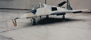Small jet aircraft with angled surfaces in hangar. It is painted in a disruptive scheme to confuse casual onlookers.