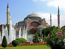 A reddish building topped by a large dome and surrounded by smaller domes and four towers