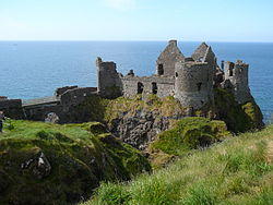 A ruin of a medieval castle on a high cliff over the sea. A round tower stands in front in the centre.