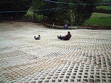 Photograph of the dry ski slope at the Mendip Snowsport Centre with two people tobogganing down the slope.
