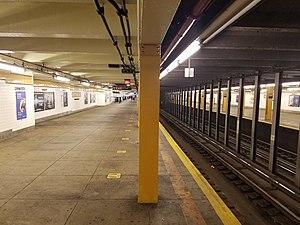 An underground train station with outer platforms. A pillar bisecting the image is painted a burnt yellow.