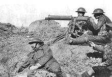 Four men in a barren landscape with a tripod-mounted machine gun