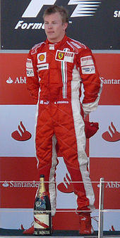 Kimi Räikkönen dons red fireproof overalls as he stands on a podium with a bottle of champagne