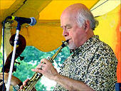 A man wearing a patterned dress shirt, performing a wind instrument while standing behind a microphone