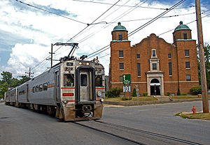 Silver single-level electric passenger train on the street in front of a brick church in Michigan City, Indiana