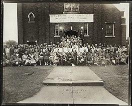 Delegates to the Amherstburg Regular Missionary Baptist Association standing in front of First Baptist Church in Amherstburg, Ontario. There is a banner on the church that states "Welcome Delegates Amherstburg Regular Missionary Baptist Association."