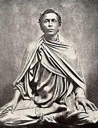 Sri Lankan man dressed in dark robes, sitting in meditation posture.