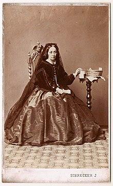 A middle-aged sad woman wearing a long weil sits in a chair