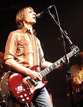 A male guitarist and singer, Mark Arm, is onstage, holding an electric guitar.