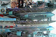 A metal-trussed hangar with a glass front and a shiny floor holds a large jet emblazoned with "United States of America" and other artifacts.