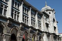 An arched neoclassical building with hanging banners, with a yellow vehicle parked in front
