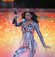 Fergie performing using a mouthpiece, and wearing a gray and silver full-bodied outfit