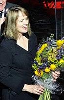 A white woman with blonde hair wearing a black shirt and holding colorful flowers.