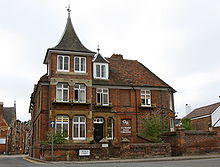 A red bricked building with a spired roof, windows and a black gate