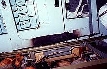 A white panel covered in buttons, which shows signs of fire damage on its bottom edge. Wiring and other pieces of hardware are arrayed beneath the panel.