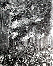Building on fire as rioters look on, one holds a sign that says "no draft"