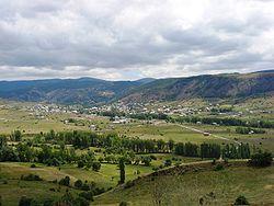 Photograph of a small town in the middle of a hilly, sparsely forested landscape.