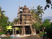Large, grey temple surrounded by people, palm trees and other vegetation