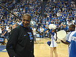 A man, wearing a black jacket and black T-shirt, is walking onto the basketball court.