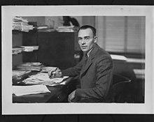 Man sitting at a desk full of papers / Homme assis à un bureau plein des papiers