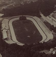 Aerial view of a concrete banked oval stadium surrounded by a tree filled park