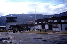 The main terminal building of an airport, with a "Penticton" sign near the entrance, as well as an "Arrivals" sign pointing to the right, with the same word written in French below it.