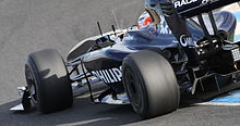 a navy open wheeled racing car drives on a tarmac course