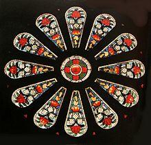 a small round stained glass window surrounded by twelve panels featuring floral designs of large red and small white flowers