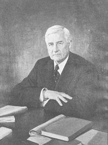 Portrait of Jesse Jones with silver hair, seated at a desk with books