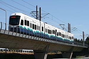 A train with two cars, traveling over a concrete bridge.
