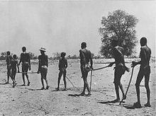 Black and white photo of children leading a line of adults across a dry landscape