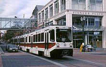 Photograph of a three-car train running along Southwest Yamhill Street with the Pioneer Place building in the background