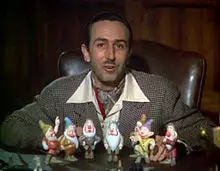 Walt Disney sits in front of a set of models of the seven dwarfs