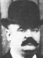Black and white photograph of a man wearing a bowler hat. He also has a thick black moustache
