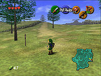 The child version of the game's protagonist, Link, stands in Hyrule field wearing his distinctive green tunic and pointed cap. In each corner of the screen are icons that display information to the player. In the upper left-hand corner there are hearts, which represent Link's health, in the lower left-hand corner is a counter that displays the quantity of Rupees (the in-game currency) possessed by the player. There is a mini-map in the lower right-hand corner, and five icons in the upper right-hand corner, one green, one red, and three yellow, which represent the actions available to the player on the corresponding buttons of the N64 controller.
