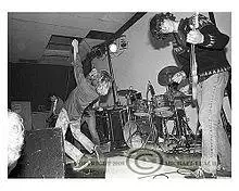 A photo of a rock band, the group Green River, performing onstage. The vocalist is arching his back while singing into a microphone. He has long hair. A male electric bass player is also visible. He has shaggy hair and is wearing jeans.