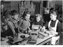 Four kindergarten children play with toy trucks on a table and a teacher sits with them while they play