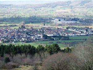 Multiple houses in Lower Langford, mostly with red roofs seen in a valley between the vegetation in the foreground and the hills beyond.
