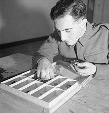 A man sorts small objects into a wooden tray