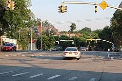 A road during the morning with a few cars and lined with shops.