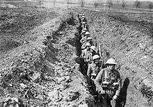 A file of soldiers from the King's Liverpool Regiment march down a shoulder-deep trench.
