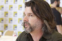 A man with shoulder length hair is looking towards the camera.