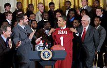 President Obama receives an Alabama jersey at the White House with various team members and coaches present.