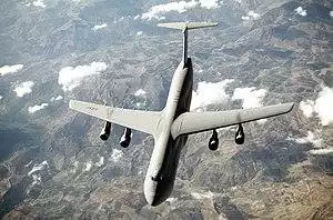 Top view of four-engine jet transport in flight above mountain range.