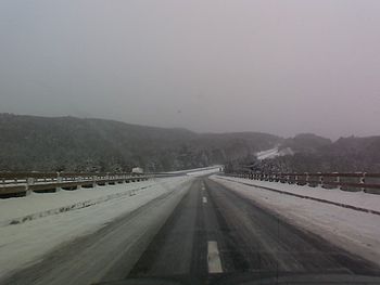 A snowy highway road that is icy and looking towards forests and mountains.